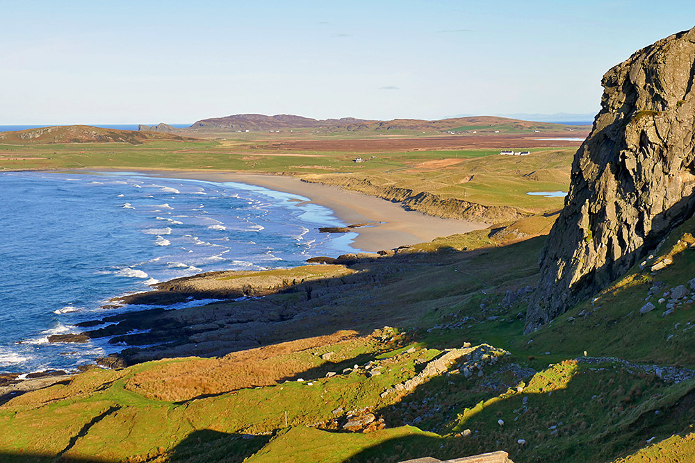 Picture of a long sandy beach below some steep rocky crags