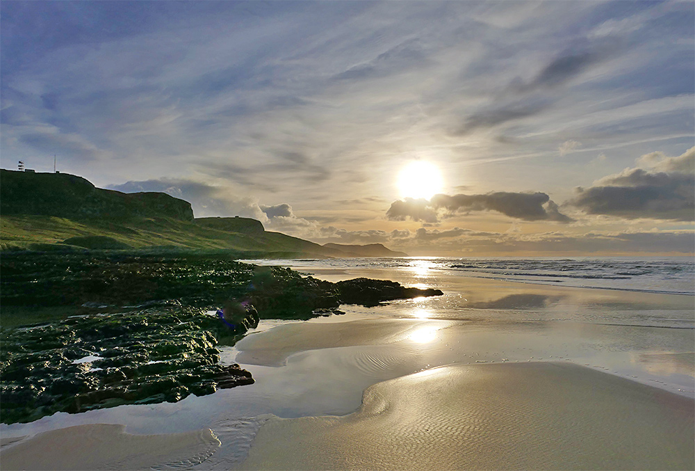 Picture of the low November afternoon sun over a sandy beach next to a rocky rugged shore