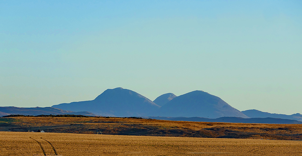 Picture of three distant mountains behind a field in a rolling rural landscape