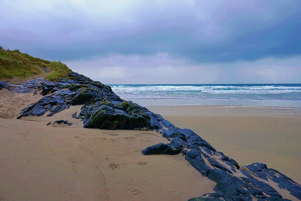 Picture of a rocky edge at the end of a sandy beach, dark clouds overhead