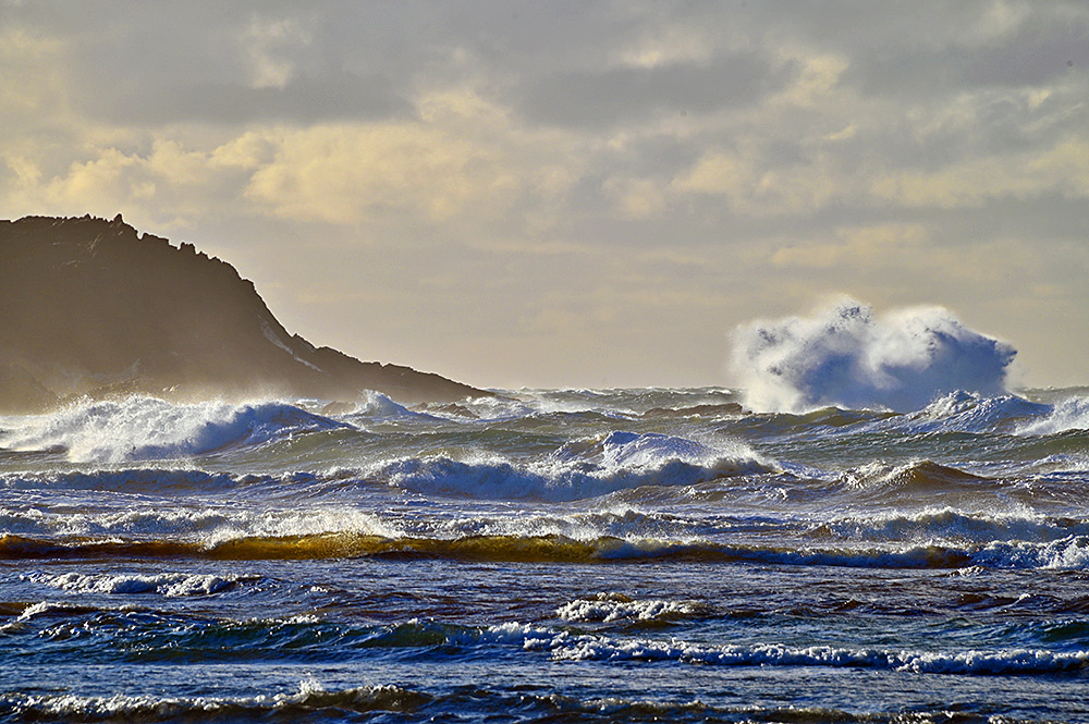 Picture of breaking waves sending spray high into the air next to a rocky shore