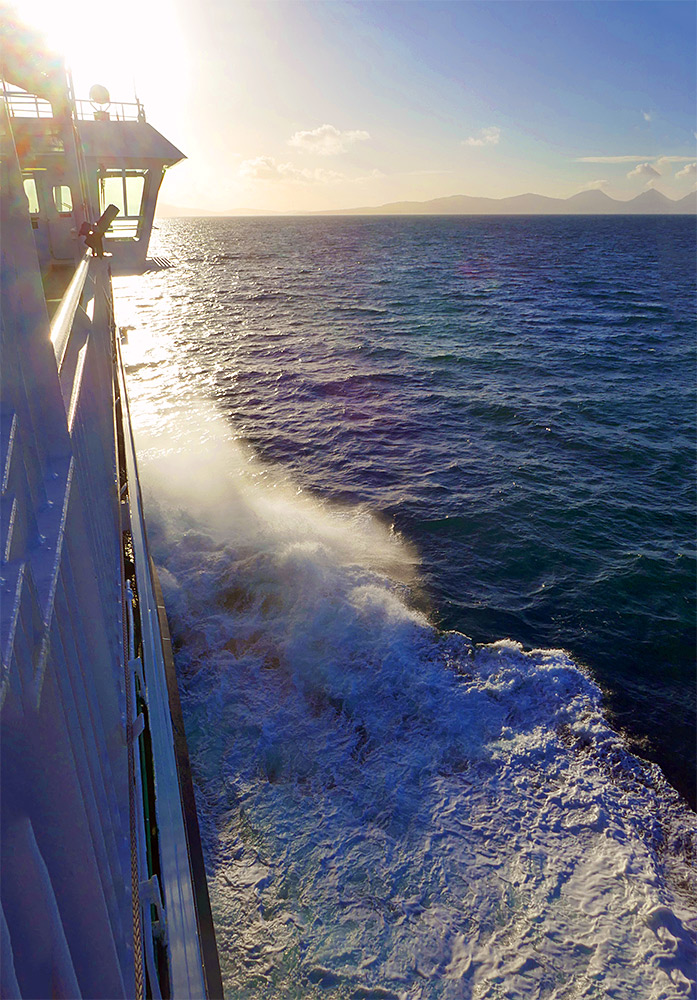 Picture of a Calmac ferry pushing through waves and into the sunshine ahead