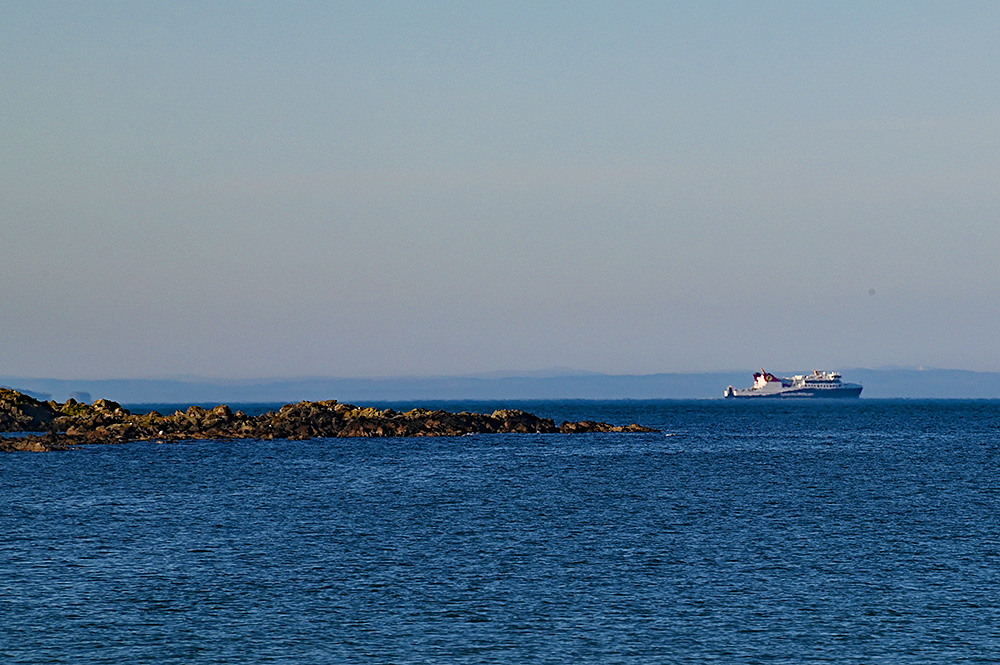 Picture of the Calmac ferry MV Isle of Islay seen in the distance off a rocky shore