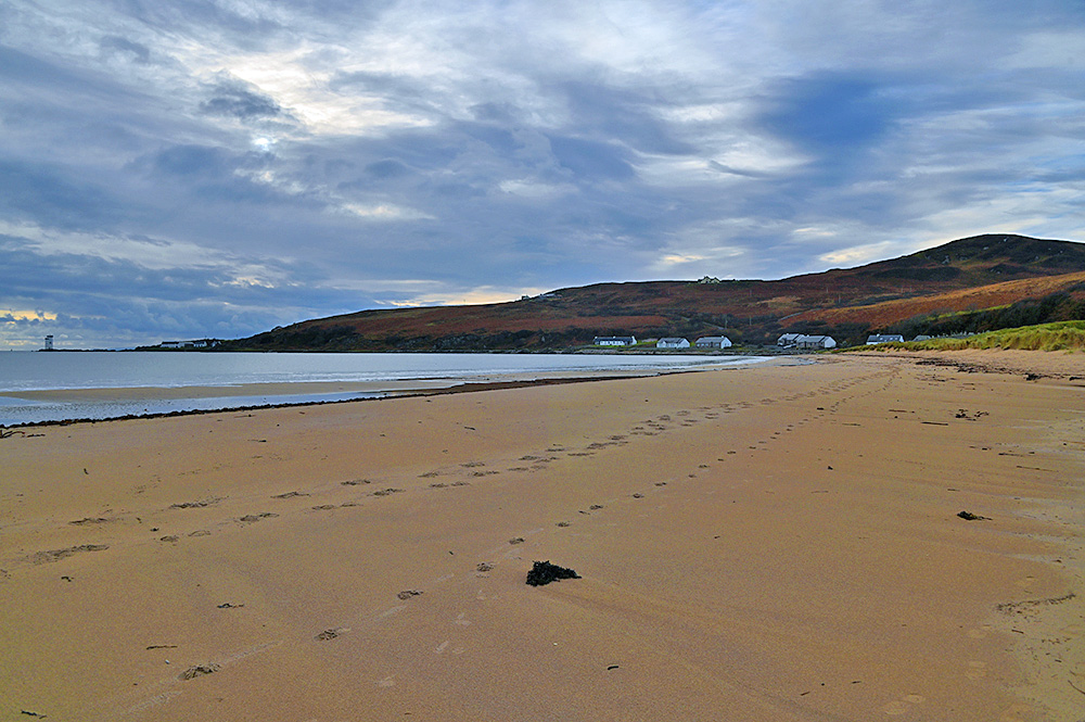 Picture of a view along a sandy beach in a wide bay, a square lighthouse visible at the end of the bay
