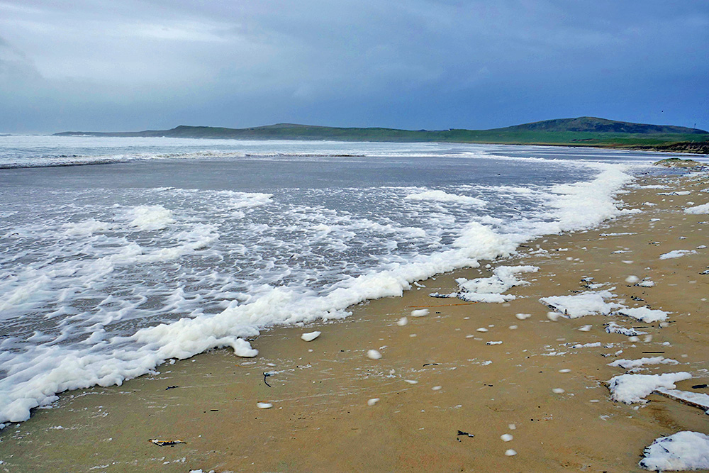 Picture of a wide sandy beach mostly covered in sea foam