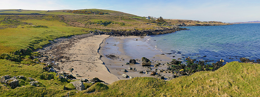 Panoramic picture of a small beach on a sea loch, seen from a hillock at the end of the beach