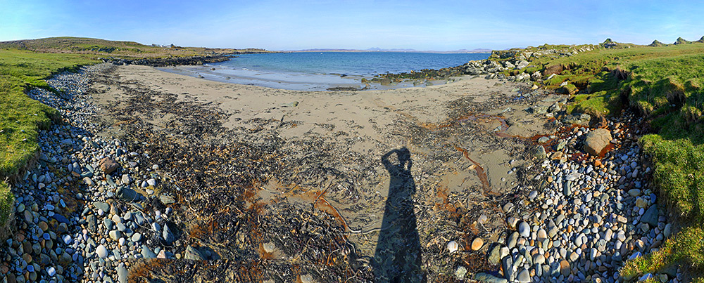 Panoramic picture of a small sandy beach at a sea loch, rocks