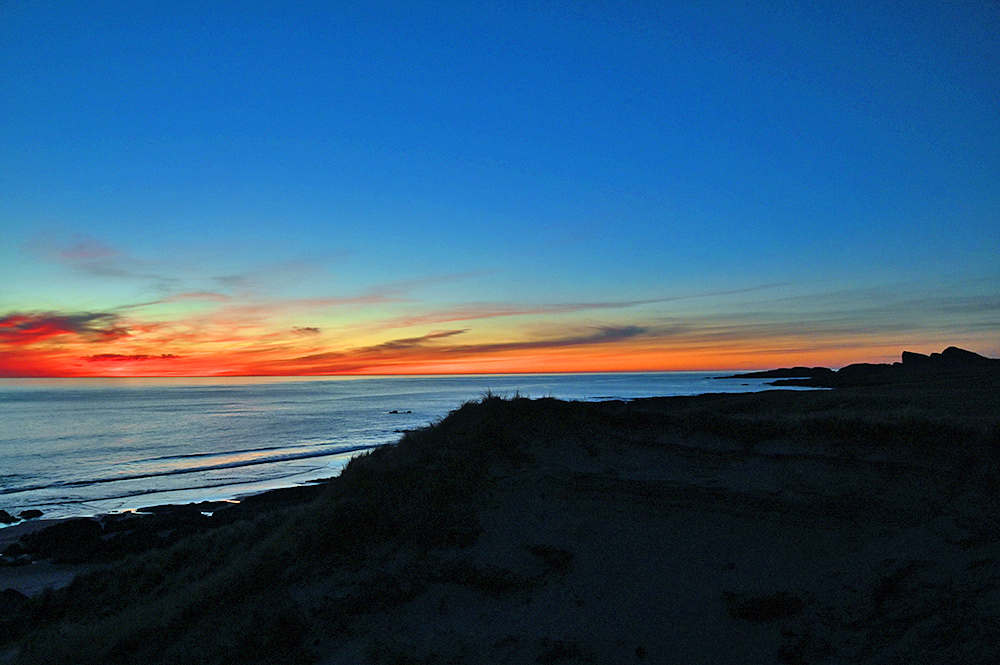 Picture of a colourful gloaming after the sunset seen from some dunes above the sea