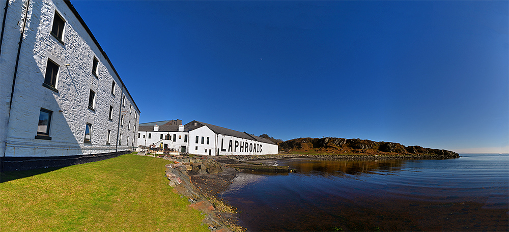 Panoramic picture of a coastal distillery (Laphroaig on Islay) on the shore of a sea loch under a bright blue sky