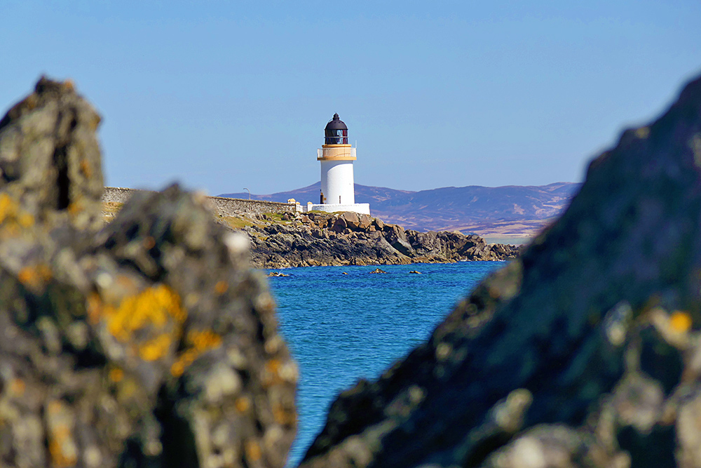 Picture of a small lighthouse on a rocky shore seen through some jagged rocks