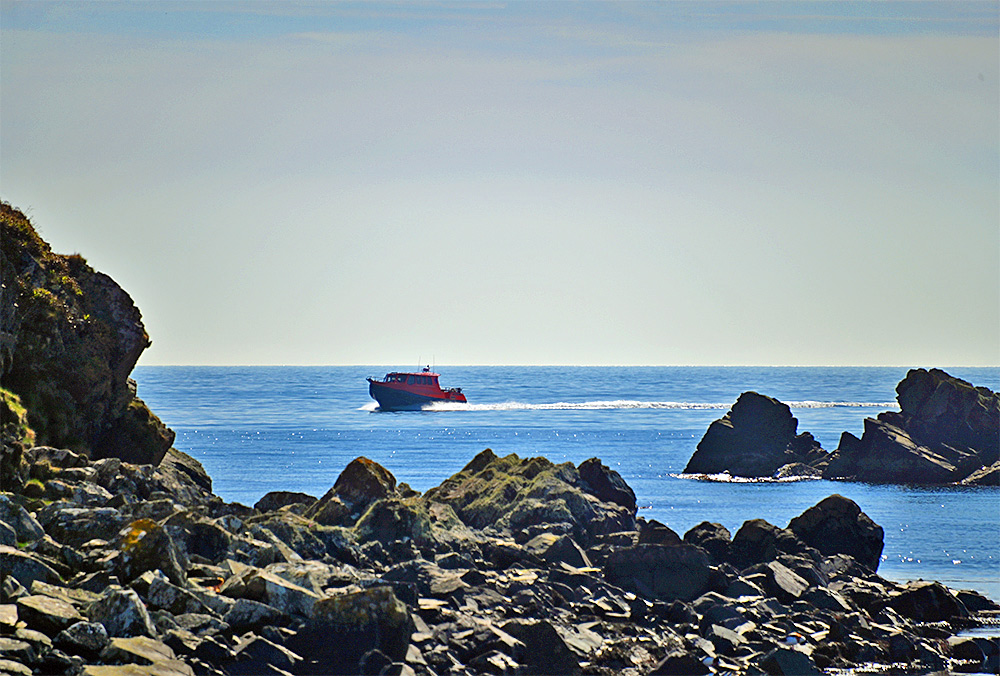 Picture of an orange motorboat with a small cabin passing a rocky shoreline
