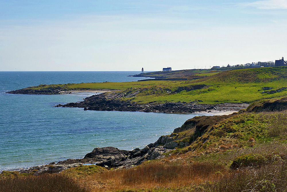 Picture of a sea loch coastline with rocky sections and sandy beaches, a small lighthouse in the distance