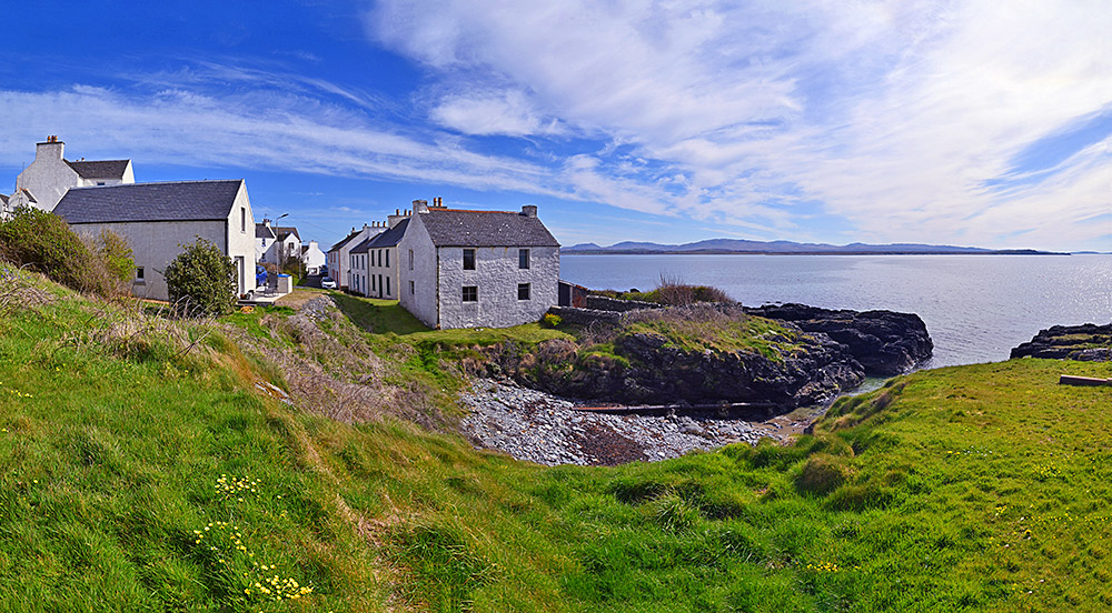Picture of white washed houses along a road in a coastal village, also a small rocky cut into the shore