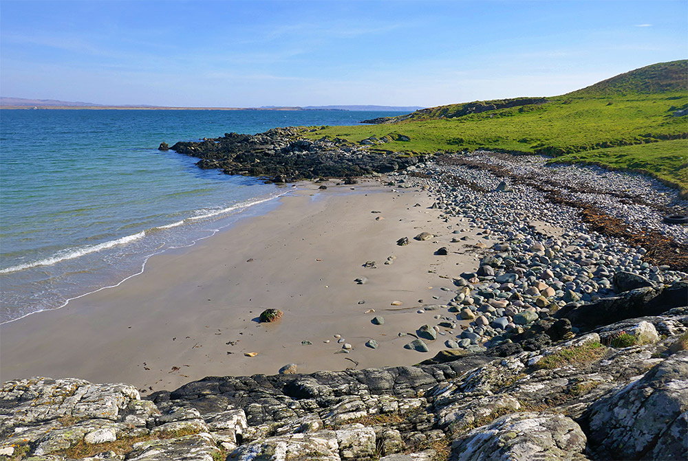 Picture of a small sandy beach with stones at the end at a sea loch