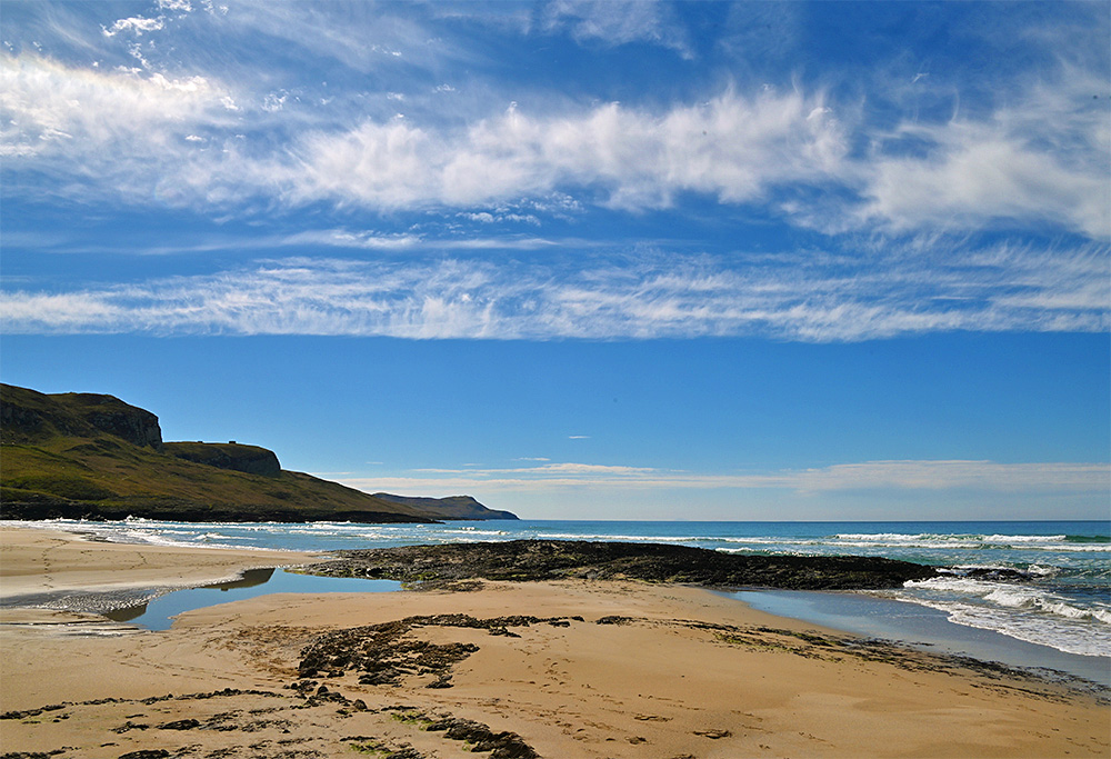 Picture of some cirrus clouds over a rocky outcrop on a sandy beach with some steep crags at the end
