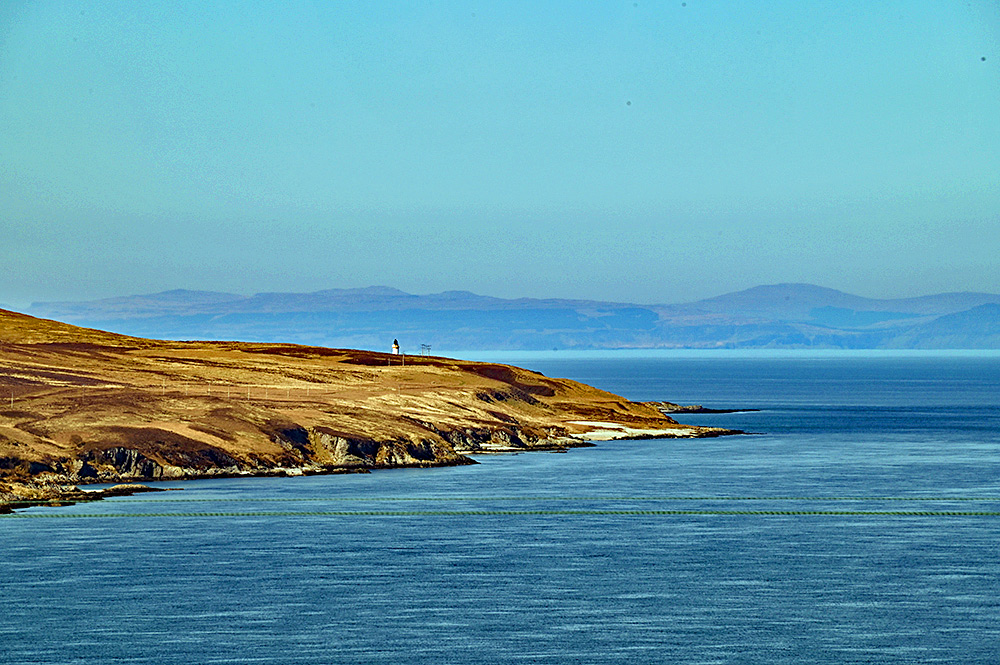 Picture of a lighthouse at the end of a sound between two islands, another island in the haze in the background
