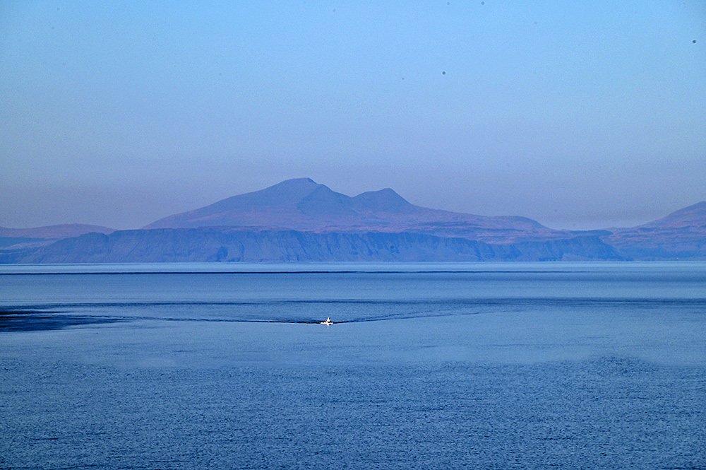 Picture of a fishing boat out on sea, islands with a mountain in the background