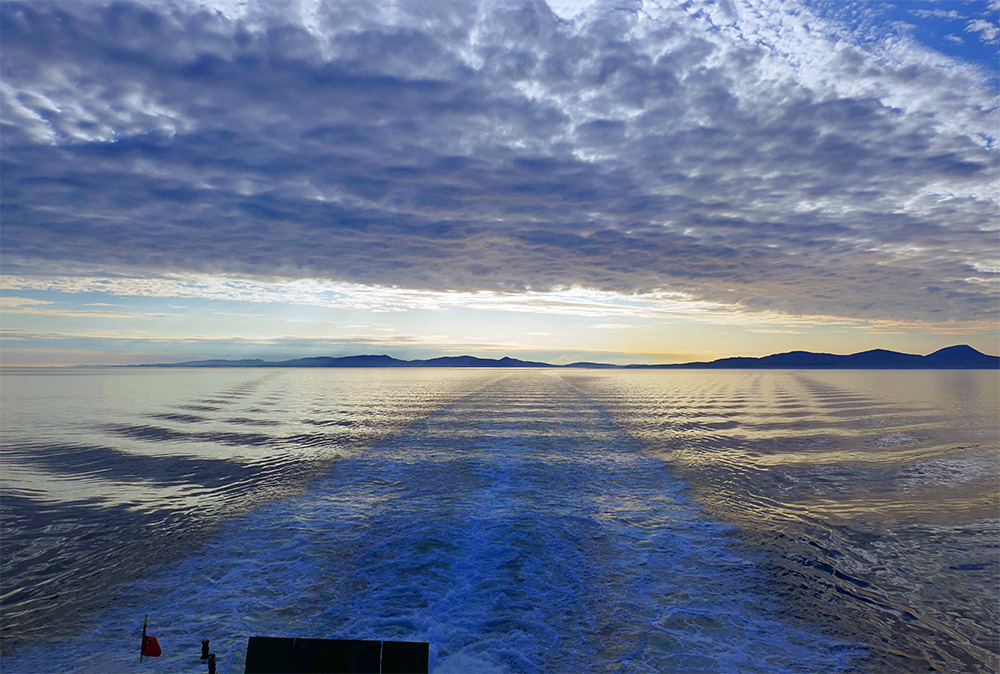 Picture of the silhouettes of two islands on the horizon, seen from the stern of a ferry
