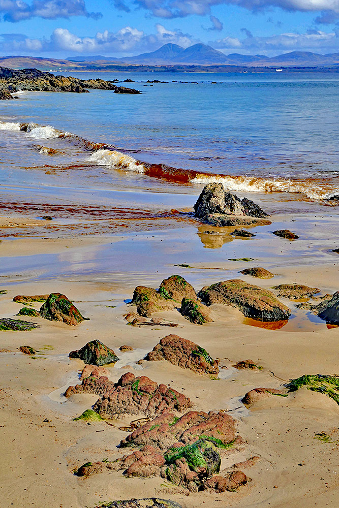 Picture of a view from a small beach across a sea loch to some distant mountains