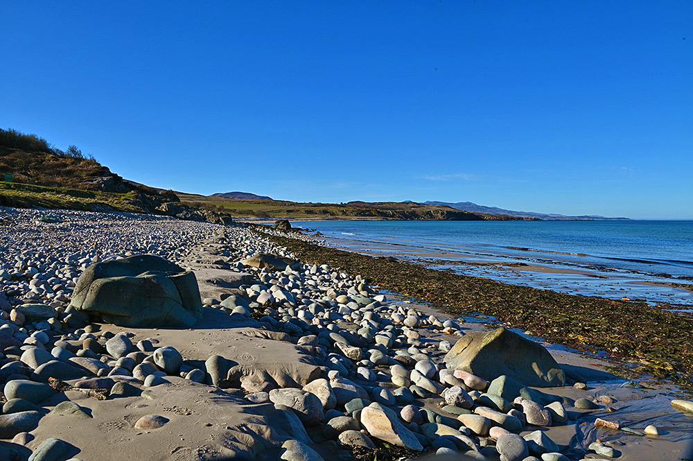 Picture of a bay with a stone/sand beach with some larger rocks on a sunny April day