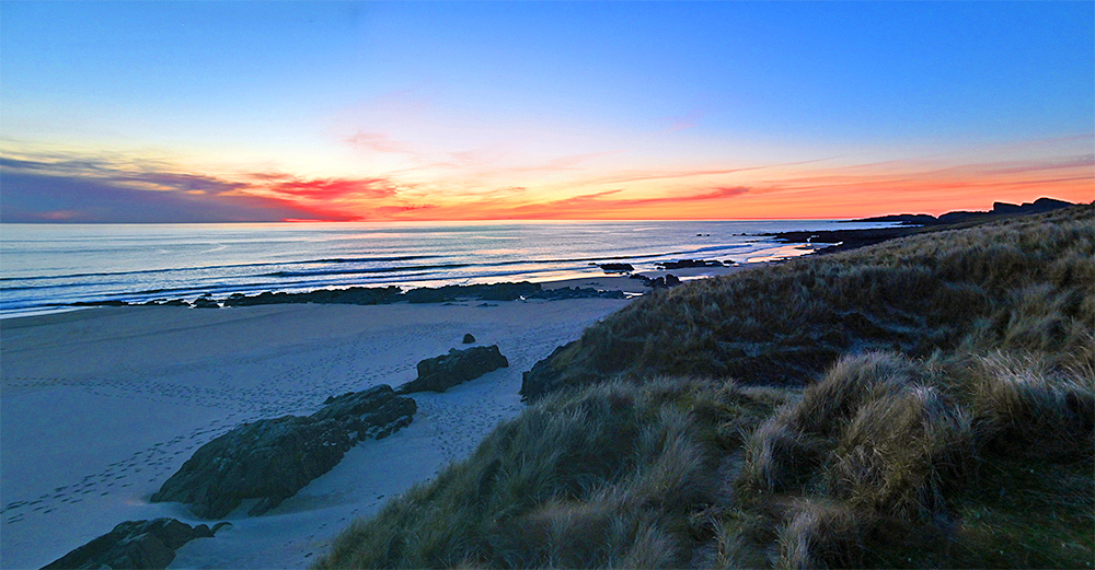 Panoramic picture of a view from dunes over a bay with a beach in the beautiful light of the gloaming after sunset