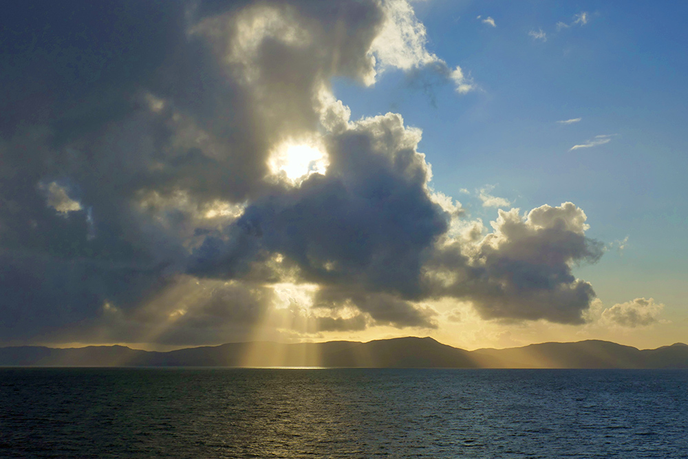 Picture of a sunburst through clouds moving in over an island