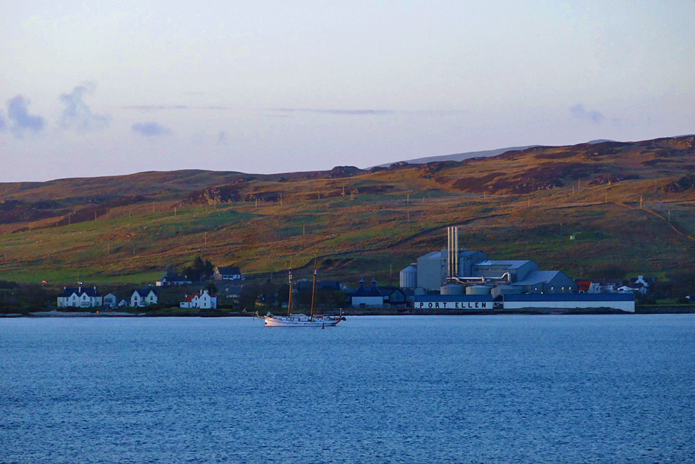 Picture of a coastal distillery and maltings with a tall ship anchored in front of it
