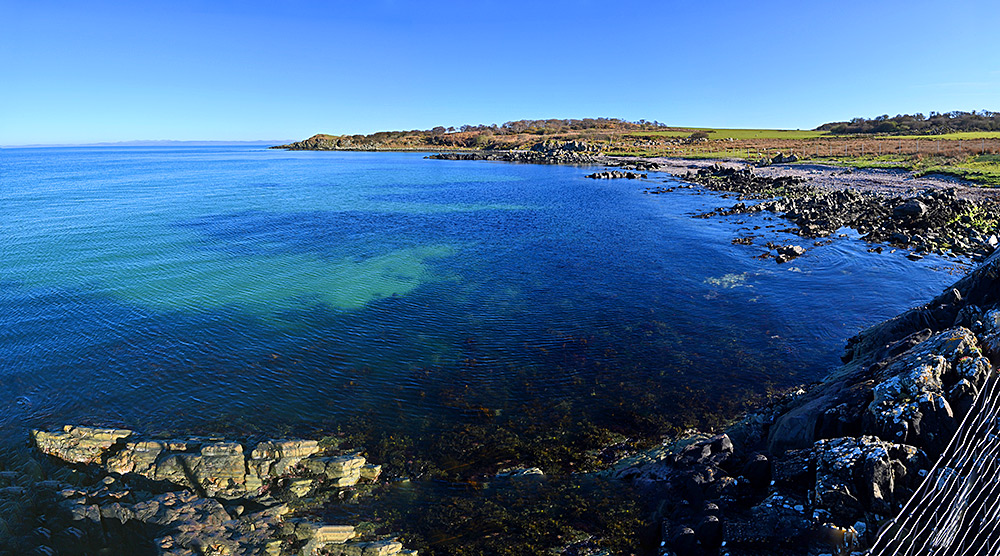 Panoramic picture of a small bay with a beach and rocks mixture shore