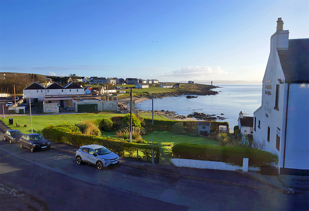 Picture of a view from a house in a small coastal village on a sunny April morning, looking over a coastline with a beach and various buildings as well as a lighthouse