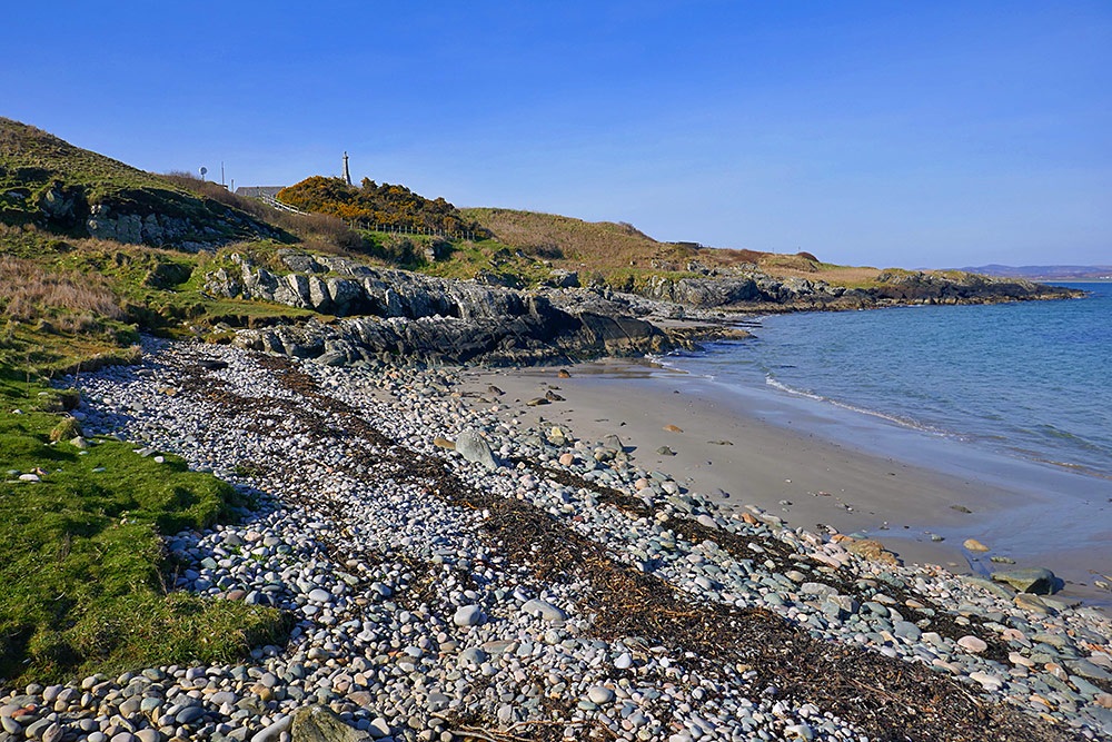 Picture of a small beach below a small war memorial surrounded by Gorse