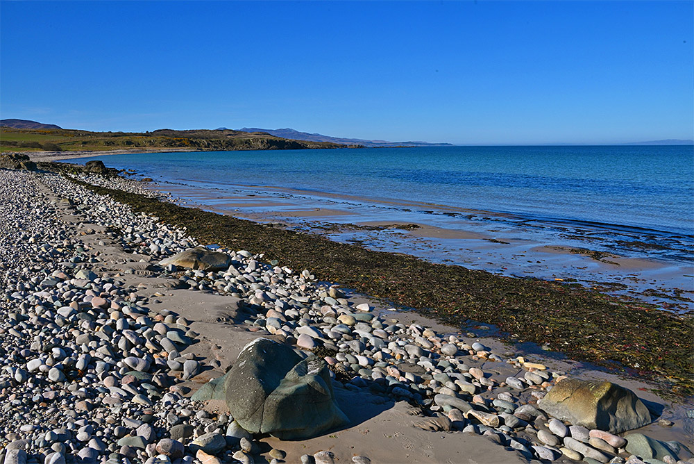 Picture of a bay with a pebble beach looking out over the sound between two islands and the mainland