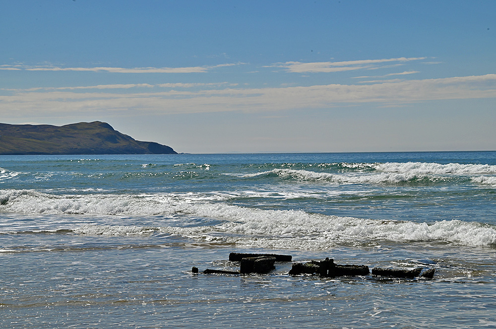 Picture of a small wreck in the surf of a wide bay with small waves rolling in from the bay