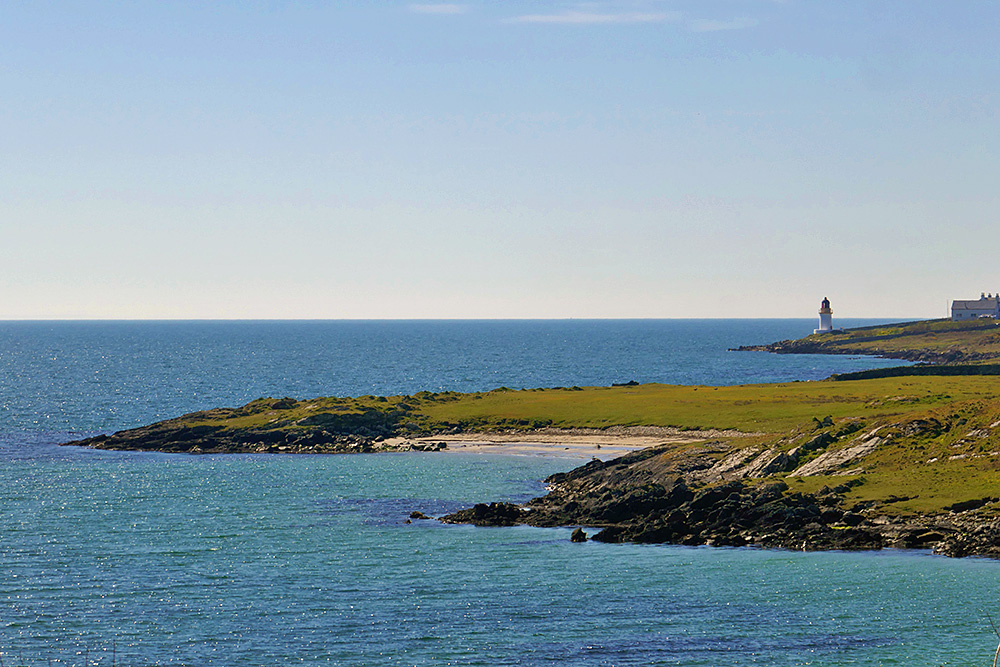 Picture of a small beach on a sea loch with a small lighthouse in the background