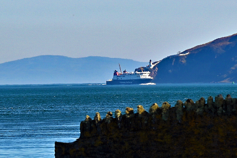 Picture of the Calmac ferry MV Finlaggan below a lighthouse, seen from the distance