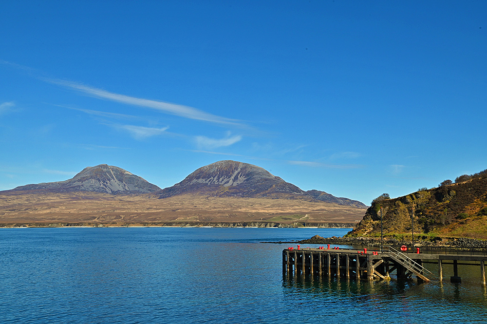 Picture of two mountains seen across a sound between two islands, a pier with red painted bollards on the right