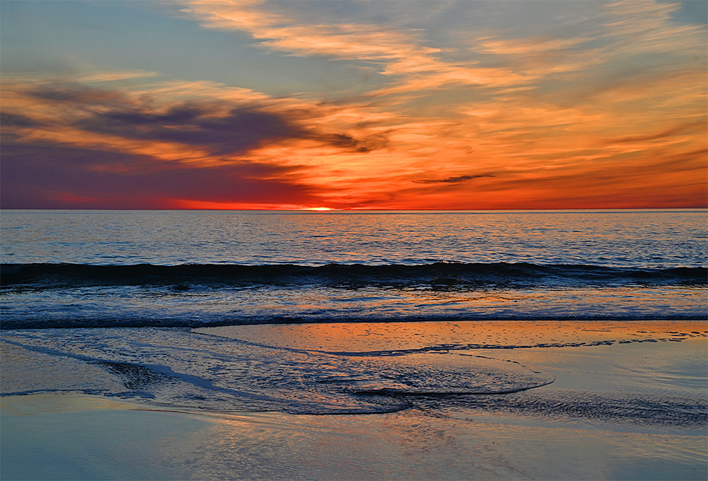 Picture of a colourful sunset with orange, red and yellow skies over a wide bay