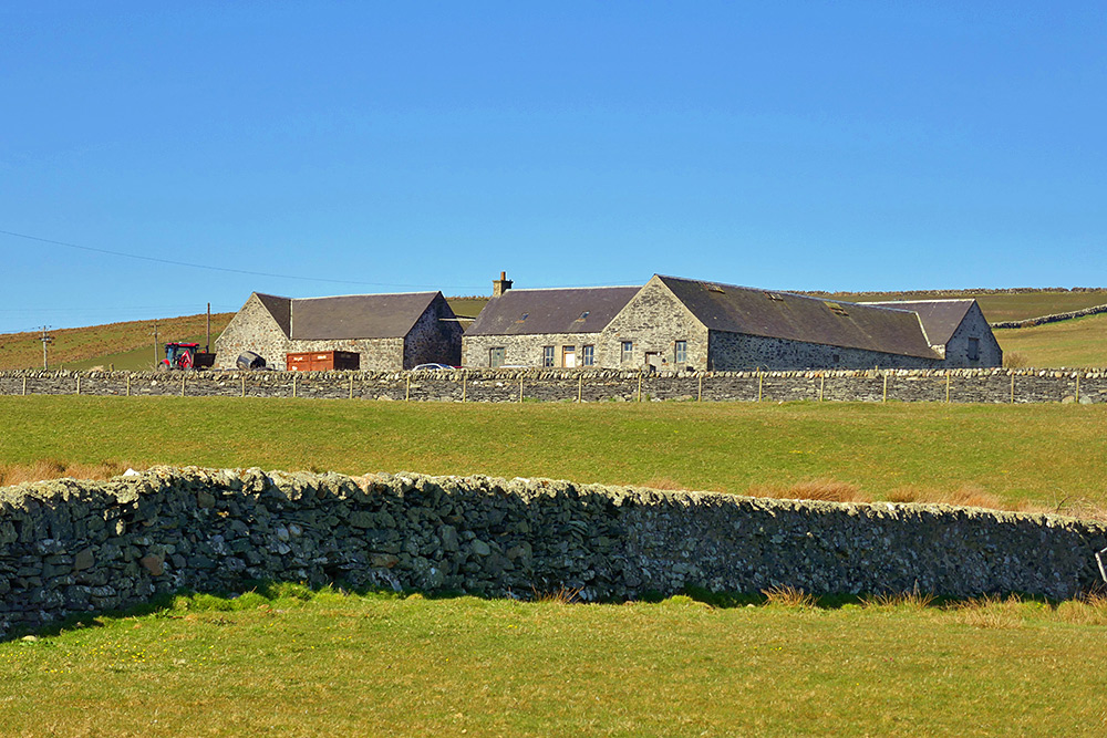 Picture of a farm building behind drystone walls on a sunny day