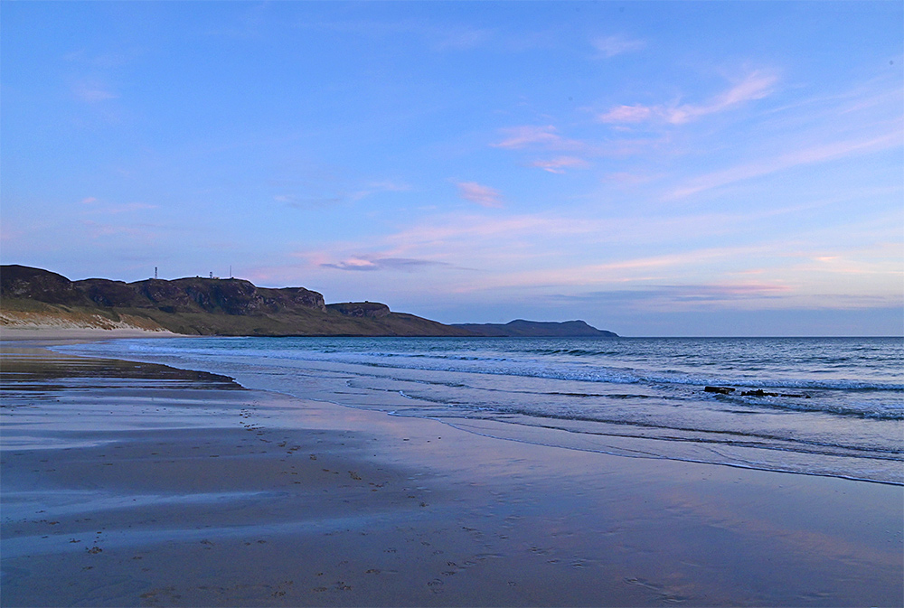 Picture of a sandy beach backed by dunes in a wide bay in the mild light of the gloaming after sunset