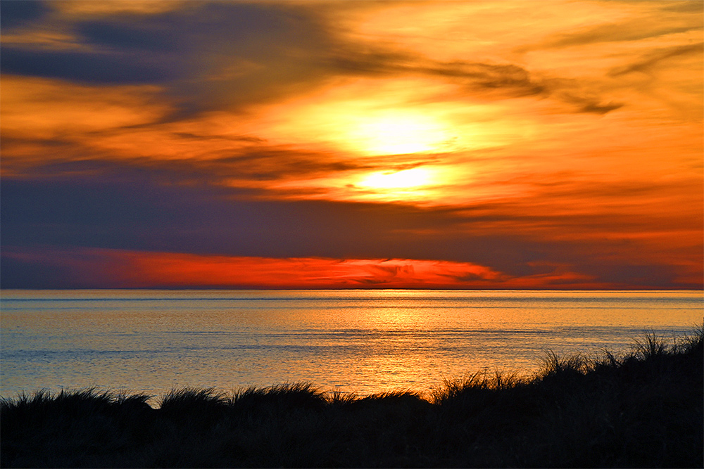 Picture of a colourful cloudy evening sky above a wide bay, seen from the dunes at the bay