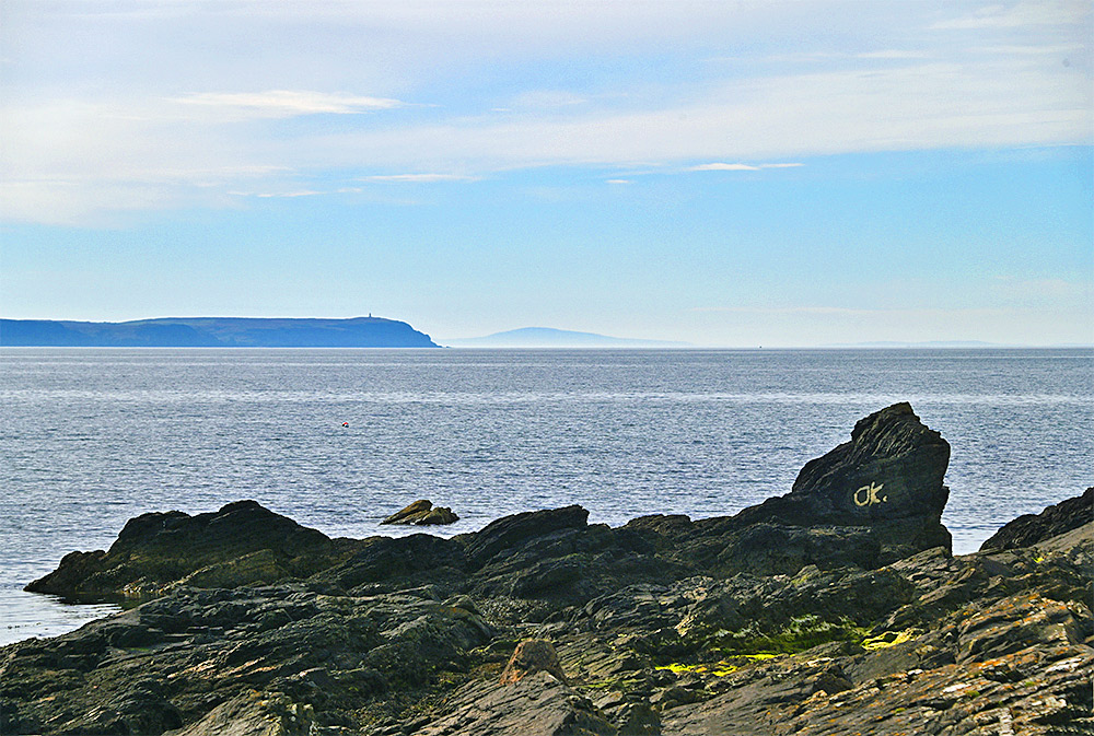 Picture of a coastal rock with the letters OK painted on it, behind it a sea loch with