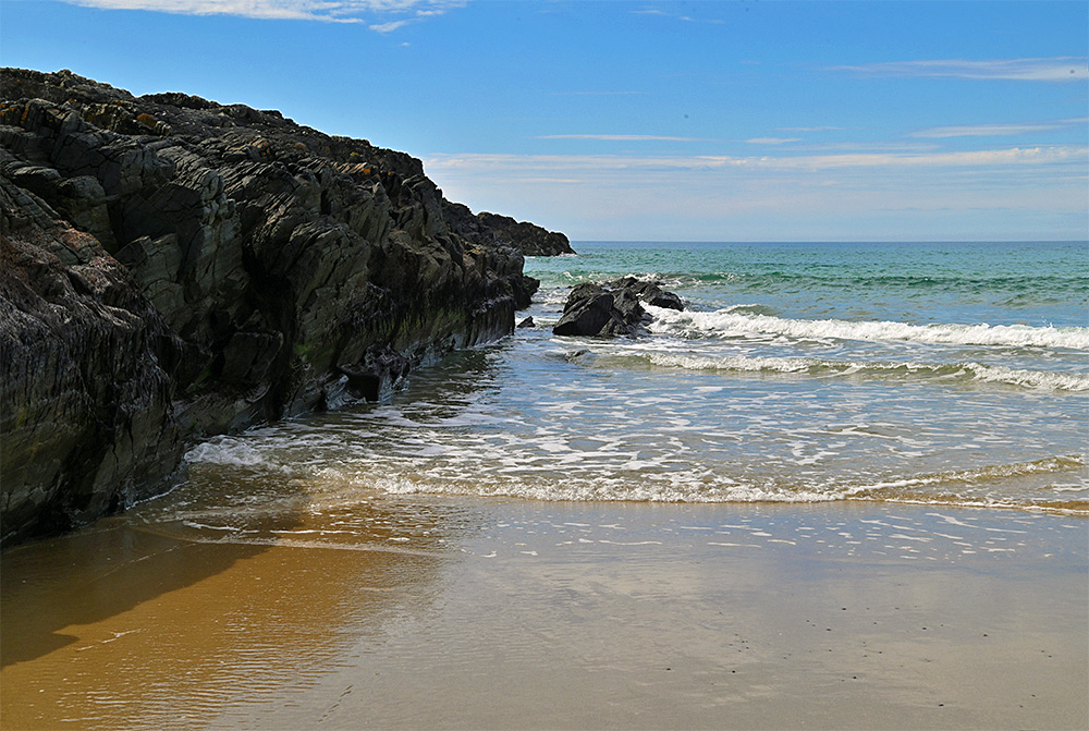 Picture of large rocks at the end of a sandy beach, some small waves rolling in
