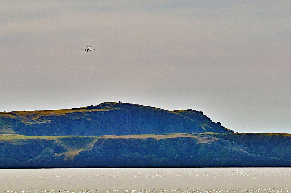 Picture of a passenger plane flying low above a small coastal hill