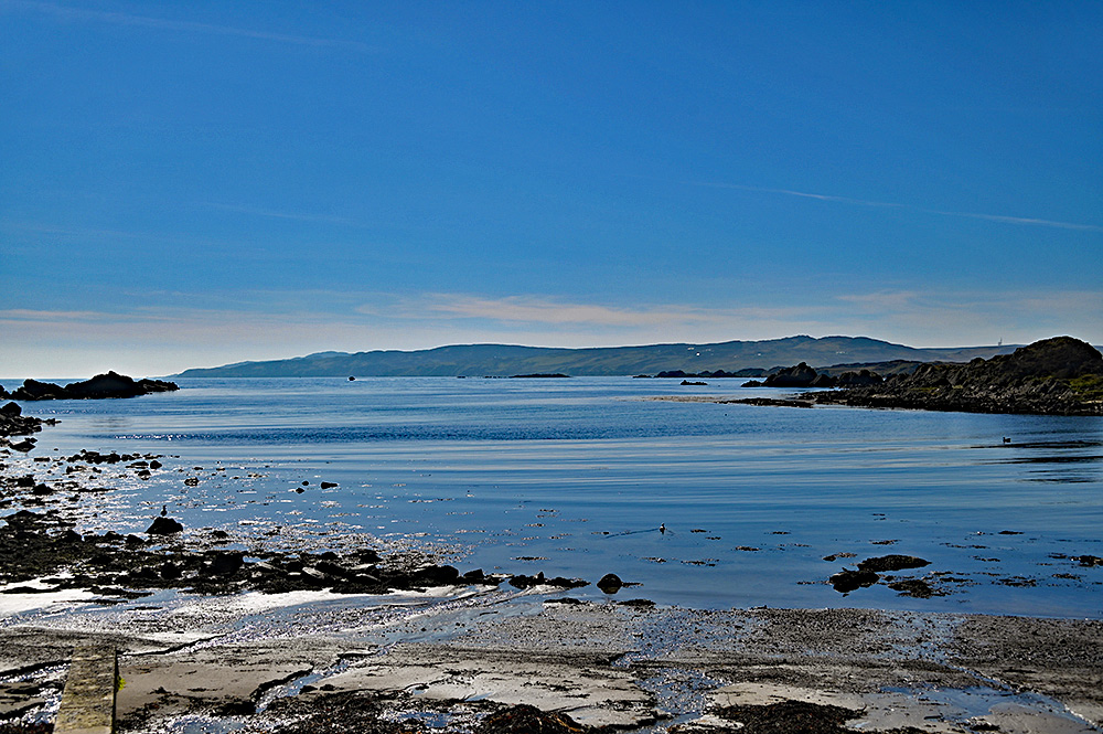 Picture of a view out of a small sea loch on a sunny afternoon to a large peninsula