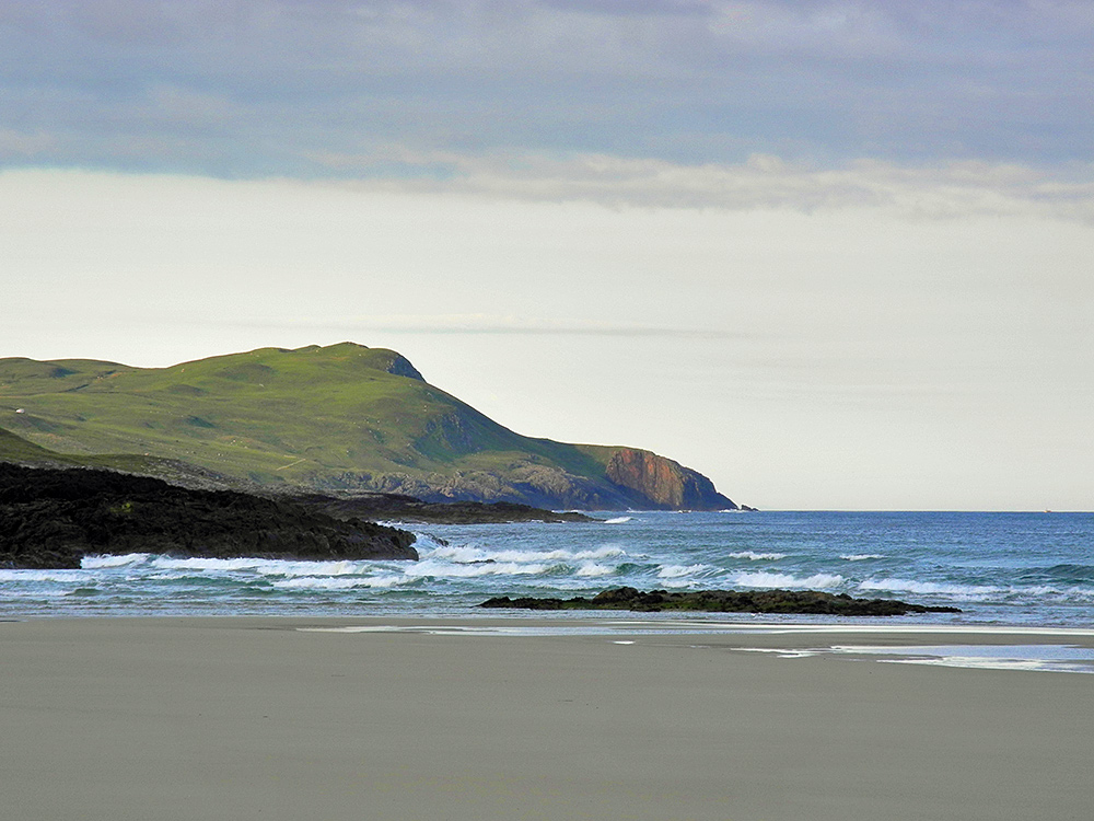 Picture of a view from a sandy beach down a rugged shoreline with cliffs and rocks
