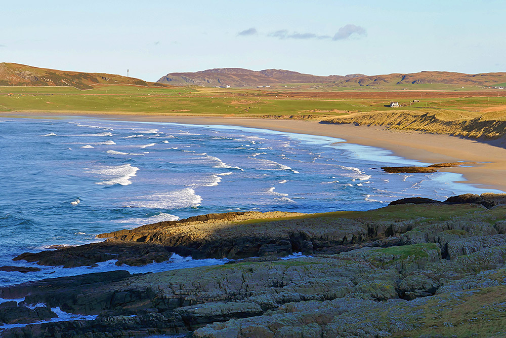 Picture of a wide bay with waves rolling onto a long wide sandy beach in some nice mild sunshine