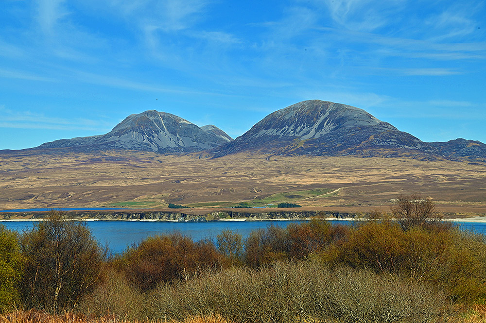 Picture of three scree covered mountains seen across a sound between two islands on a sunny afternoon