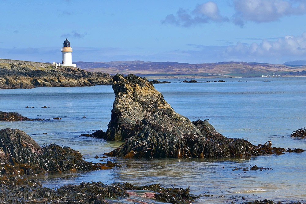 Picture of rocks at the end of a beach, a small lighthouse in the background