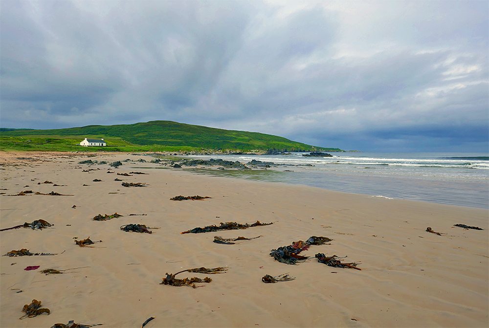 Picture of the end of a beach with a white washed cottage under a mostly cloudy sky