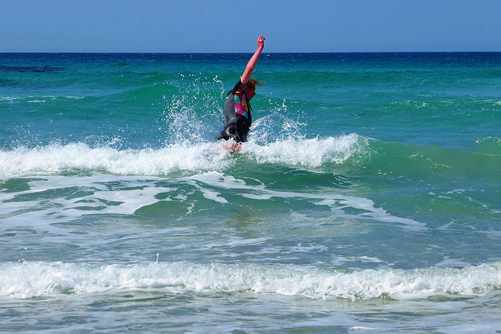 Picture of a swimmer in a wetsuit jumping through a wave in shallow water