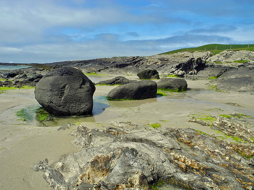 Picture of 3 large rocks in a row at the rocky end of a sandy beach